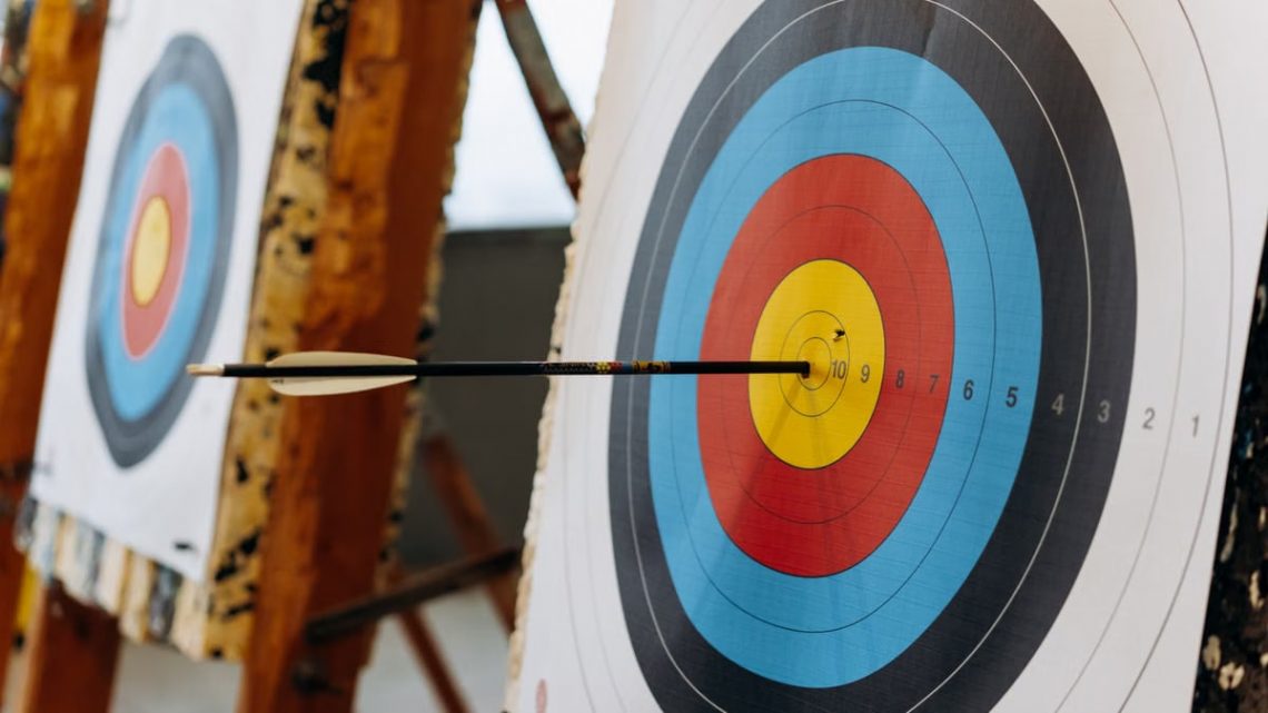 An arrow hits the bullseye on a colorful target in an indoor archery range.