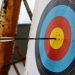 An arrow hits the bullseye on a colorful target in an indoor archery range.